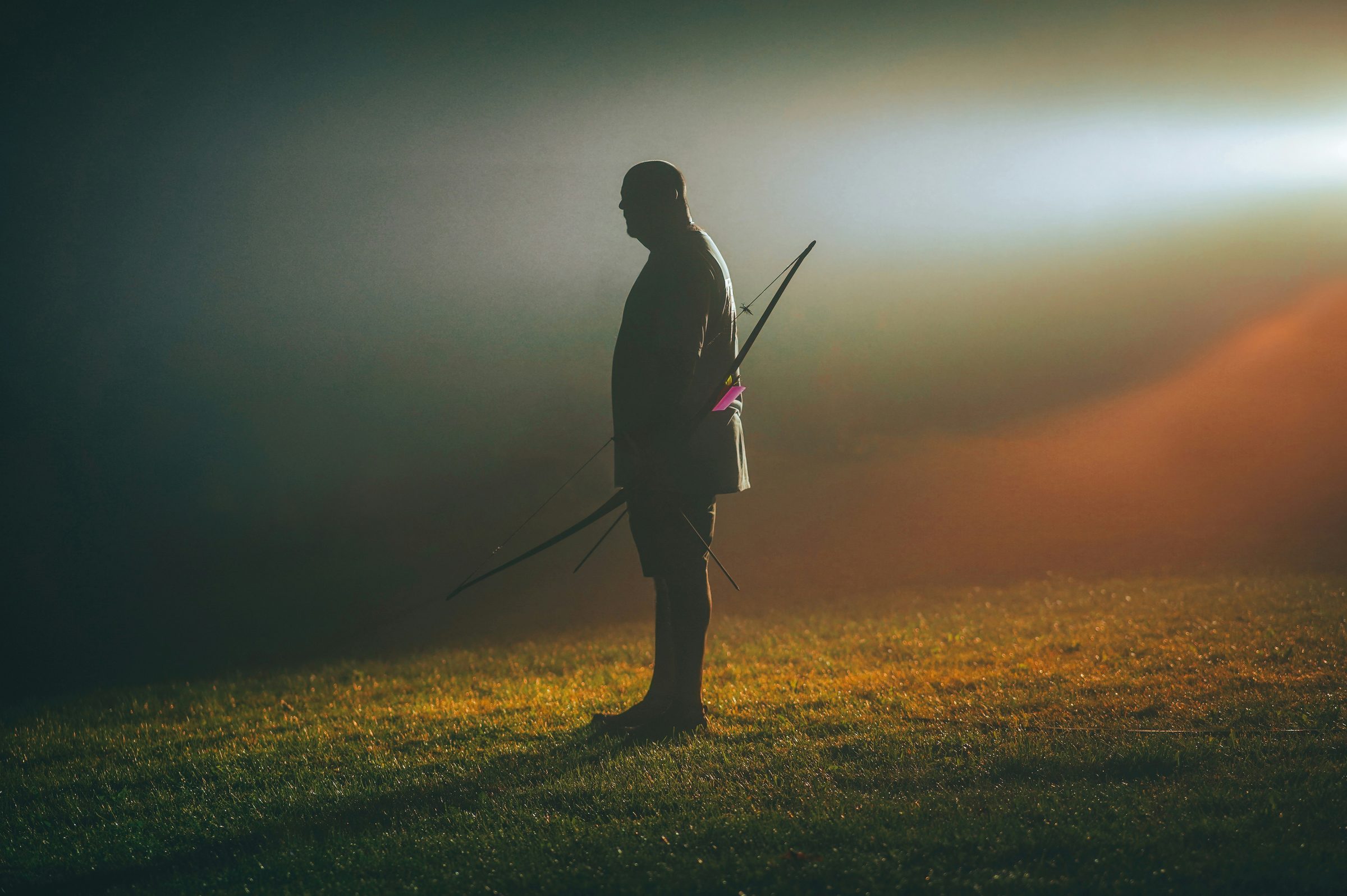 Archer silhouetted in mist at last light, traditional bow in hand