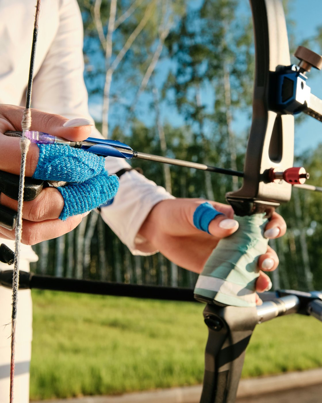 Hands nocking an arrow on a tuned recurve — grip, tab, and sight detail
